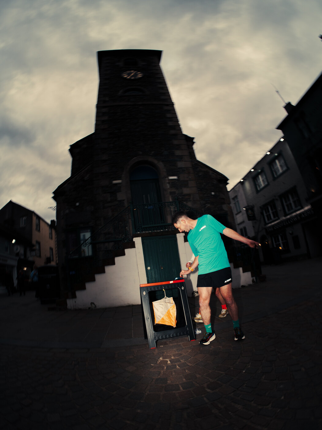 An orienteer in a turquoise shirt checking in at a control beside a stone building